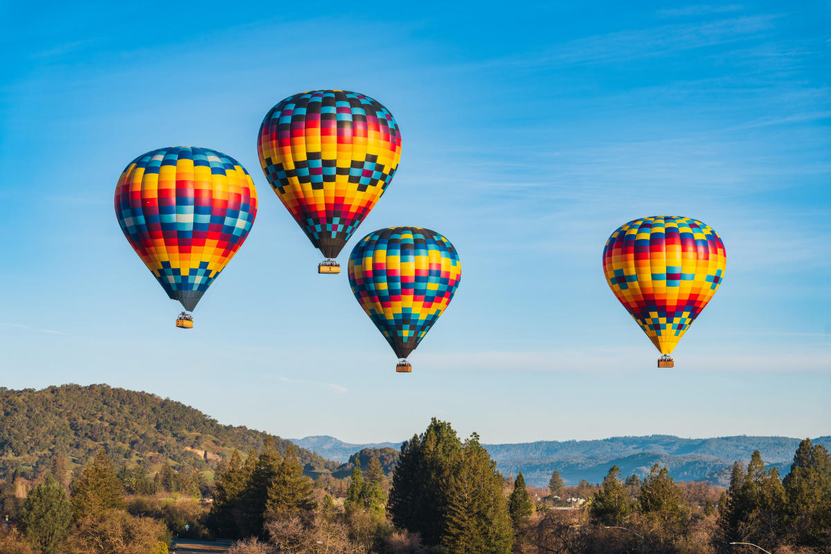 Multiple colorful balloons in flight over forested landscape